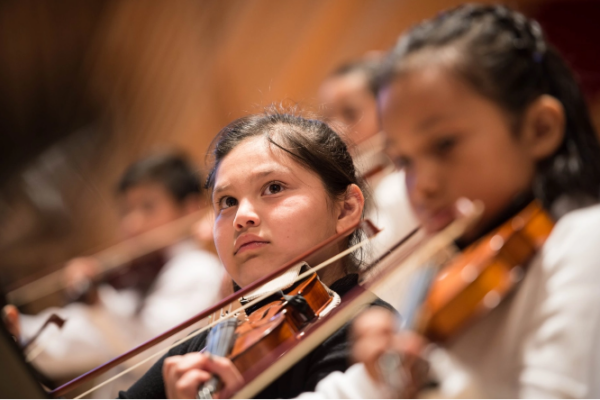 Youth violin player and other youths in soft focus around her