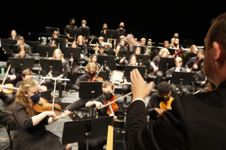 Conductor with baton on right margin at work with many teens and their instruments