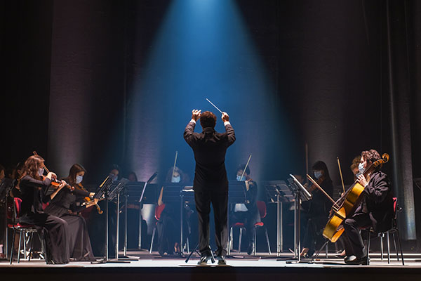 Orchestra on stage with a blue spotlight shining on the conductor.