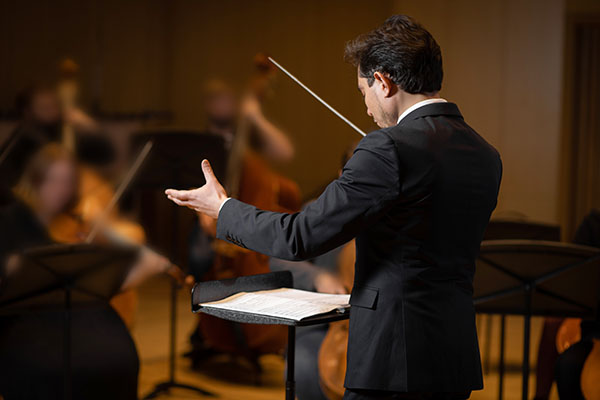 Conductor of symphony orchestra raises left hand during performance.