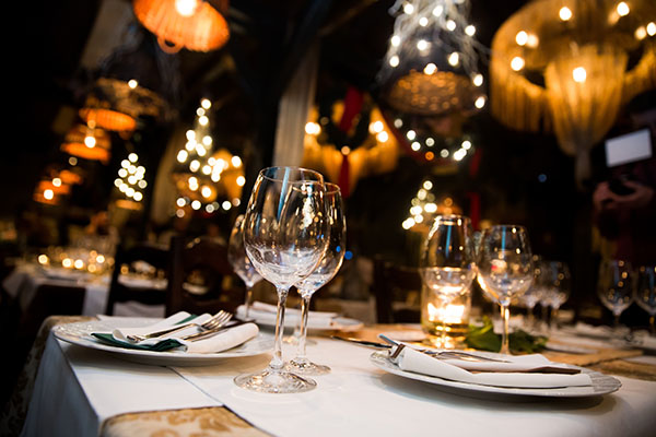 Plates and glassware on upscale restaurant table. Chandeliers hang in the background.