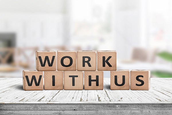 Work with us sign in a bright office environment on a wooden desk