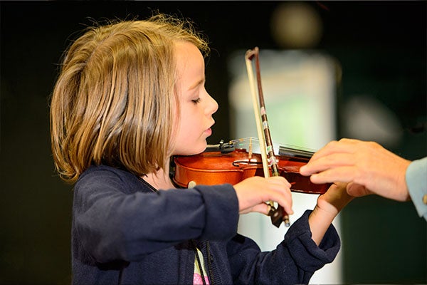 A person helping a young student hold a violin
